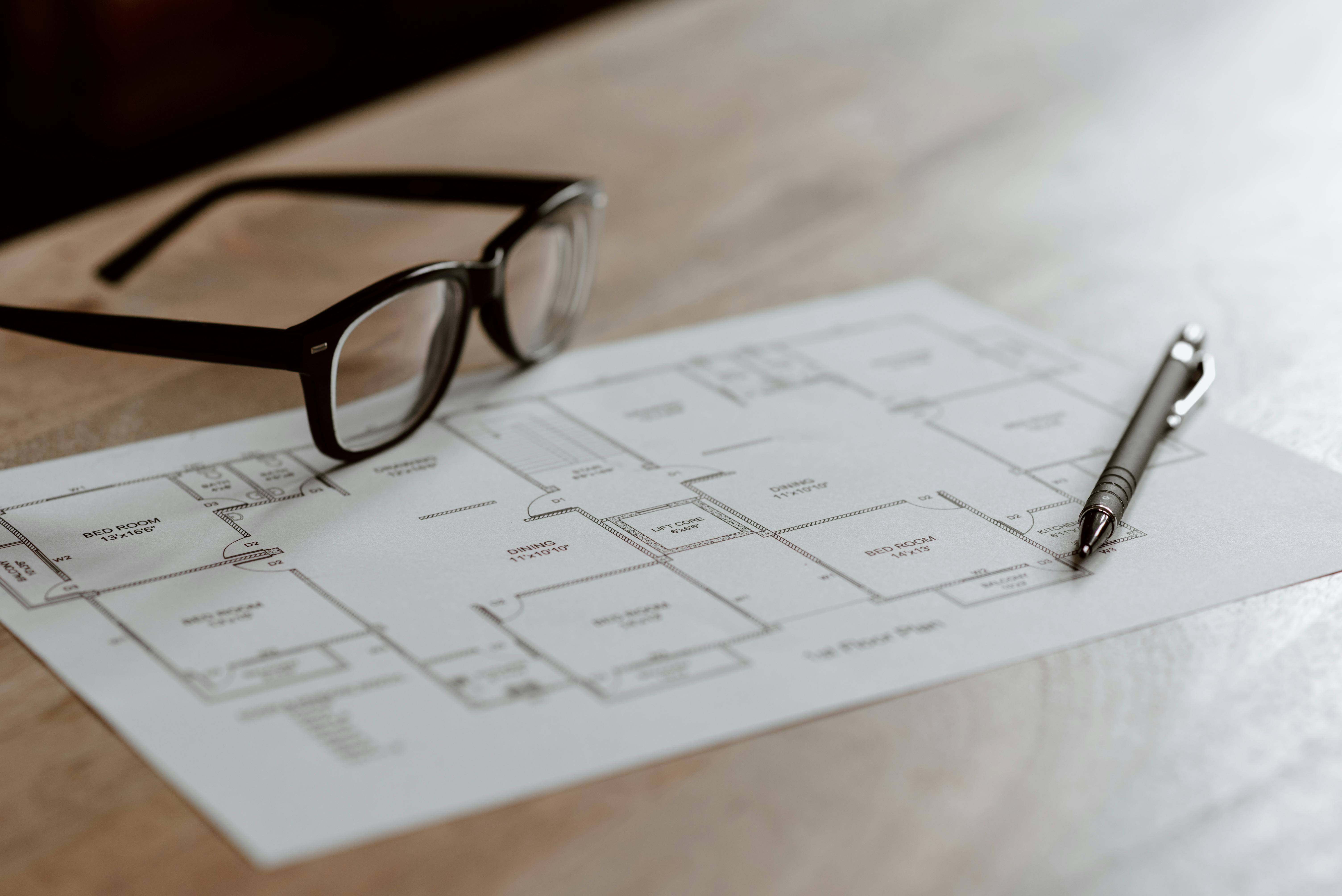 A scaled floor plan with reading glasses and a pen on a warm wood table